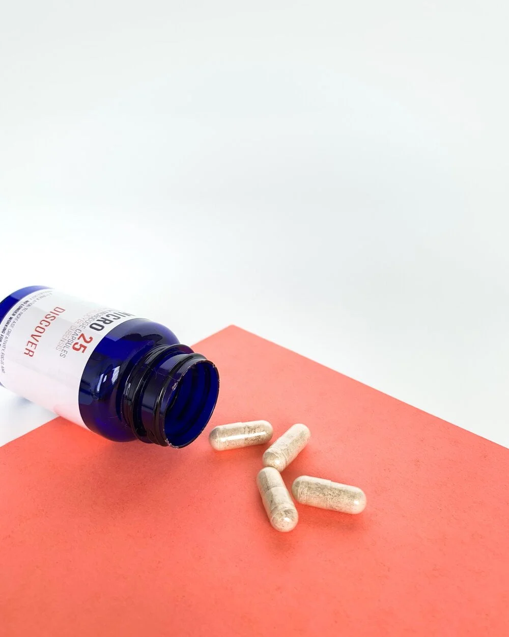 Close up of uniform clear vegetable capsules filled with a finely ground Discover blend botanical powder beside a bottle